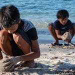 Dos niños arman bolas de arena: uno sobre la orillay el otro en arena seca